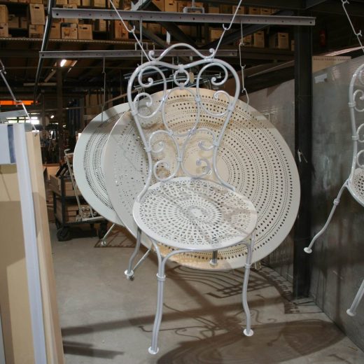 Chaises et tables blanches suspendues en atelier CRC, thermolaquage métal, équipements au fond.